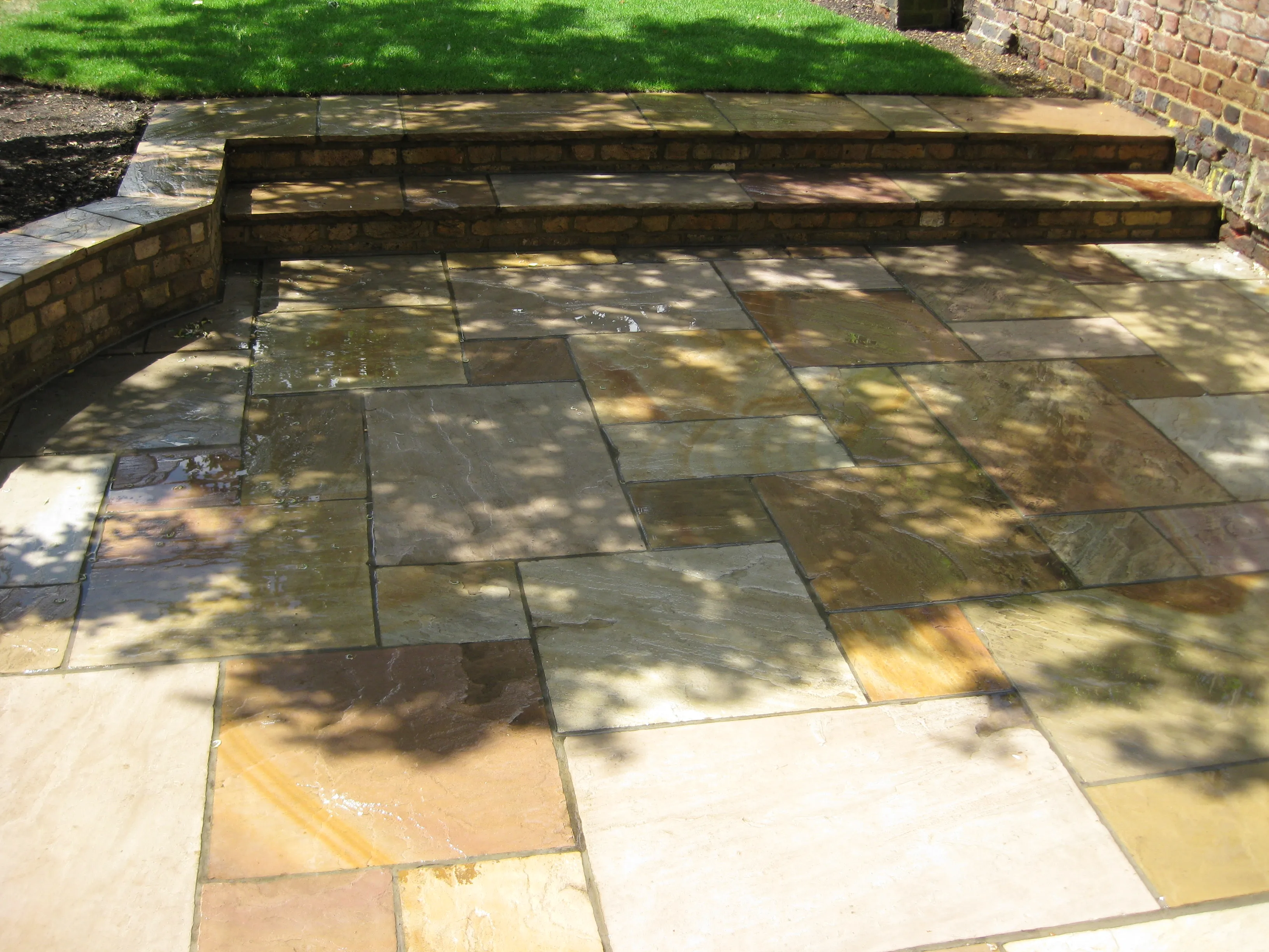 A natural stone patio with brick steps leading down to a lawn