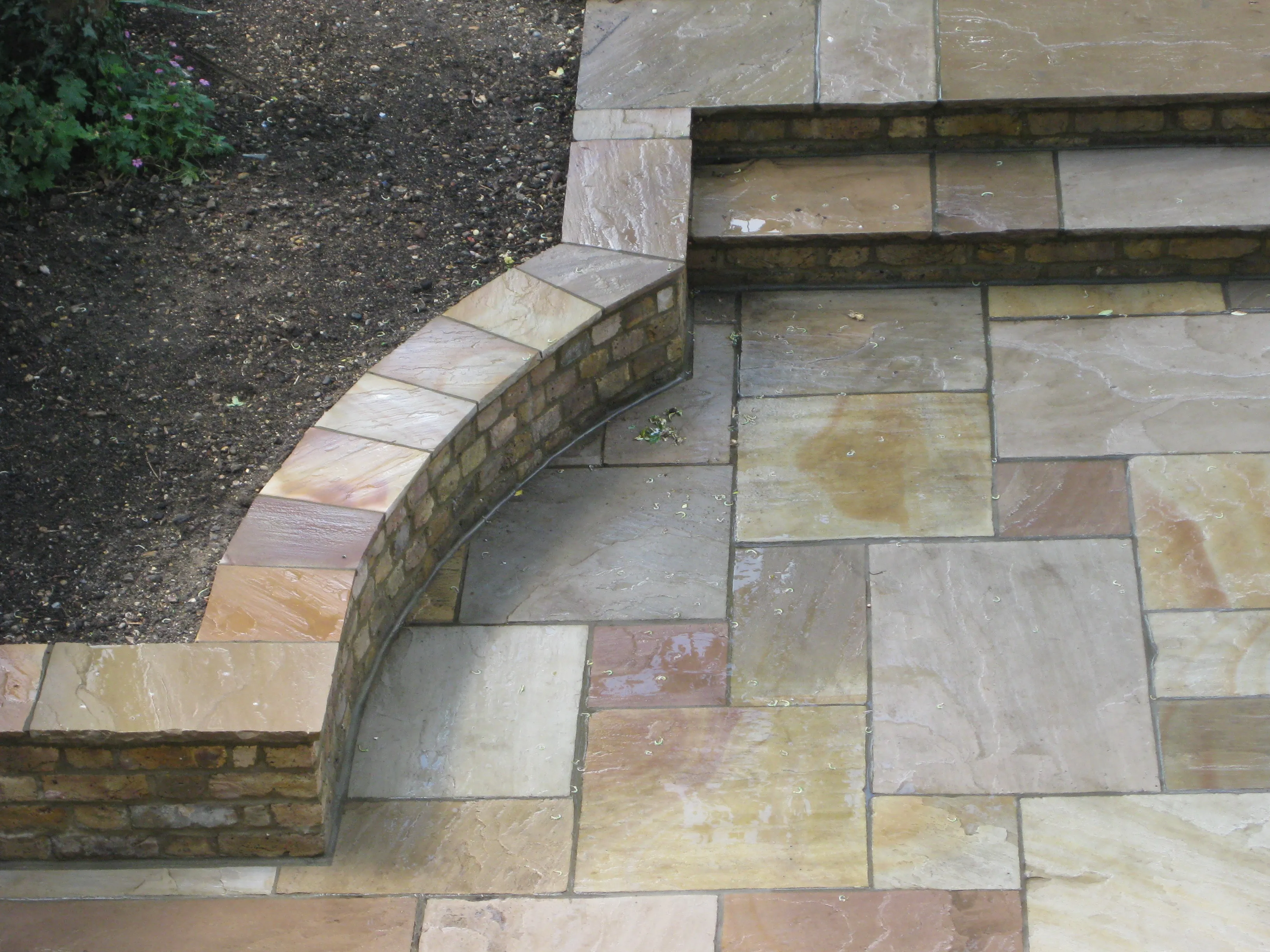 A clean natural stone patio with a curved brick retaining wall
